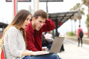 Couple surprised watching a laptop in a train station